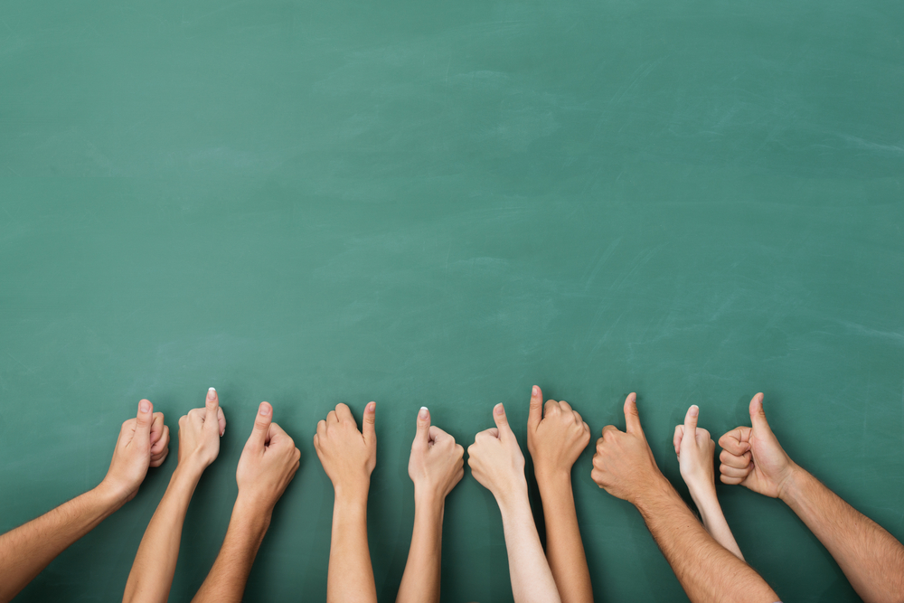 Close up view of the hands of a group of people giving a thumbs up gesture of approval an success with their hands raised against a blank green chalkboard with copyspace Close up view of the hands of a group of people giving a thumbs up gesture of approval an success with their hands raised against a blank green chalkboard with copyspace